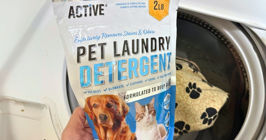 hand holding a bag of Active Pet Laundry Detergent in front of an open washing machine with a dog blanket in it