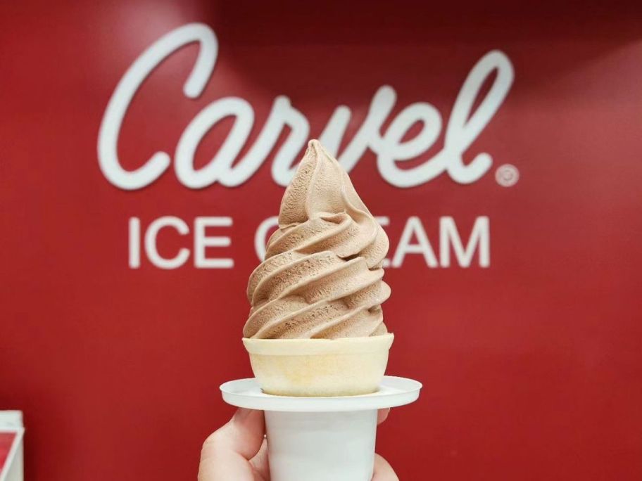 carvel soft serve ice cream cone in hand in front of carvel ice cream sign in store