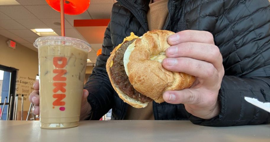 man holding dunkin breakfast sandwich with coffee on table in store