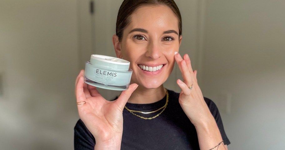 woman holding elemis cream and putting it on face