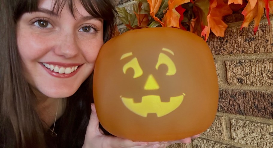 girl holding jokin pumpkin in front of fireplace