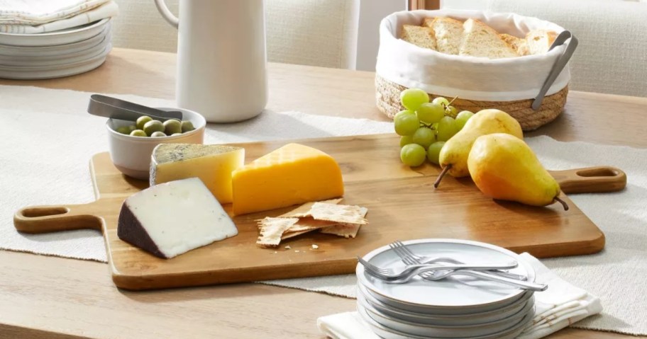 large double handle wood serving board with cheeses on it on a table with other food