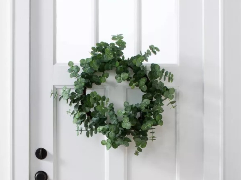 white front door with a window with a green faux eucalyptus wreath on it