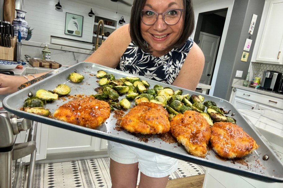 woman holding sheet pan of chicken and veggies