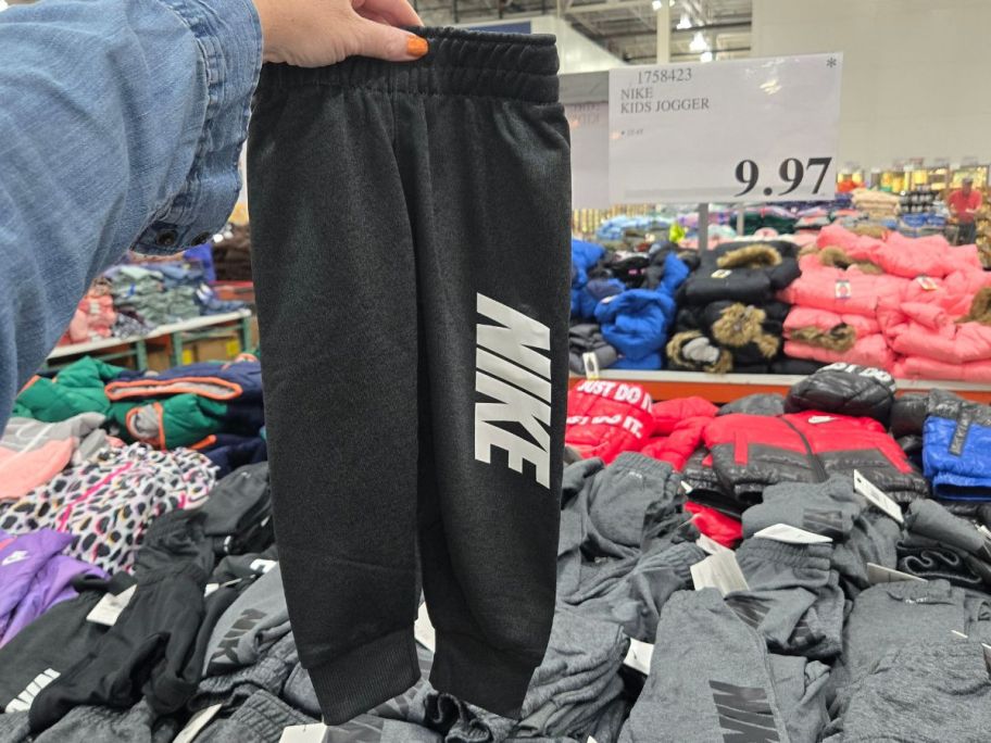 a woman hand holding a pair of kids nike joggers