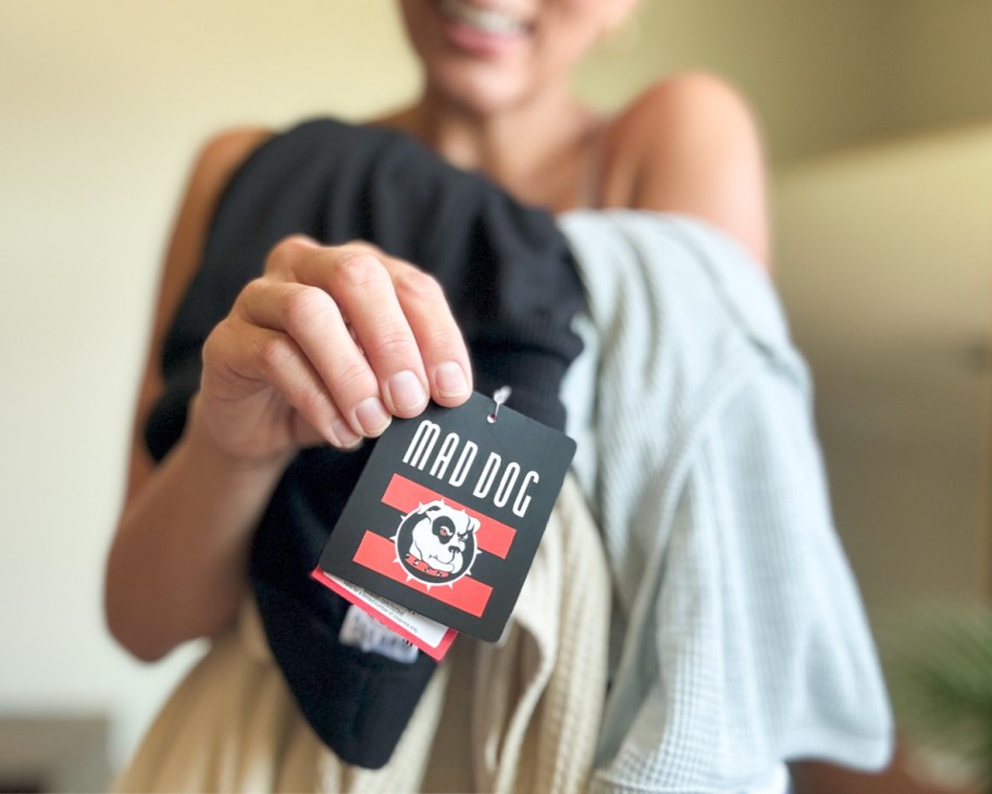 woman holding pile of mad dog clothing showing tag