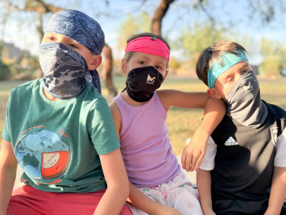 three kids sitting on bench with cooling gaiters and headbands