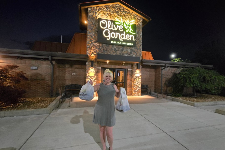 woman holding bags outside of olive garden at night
