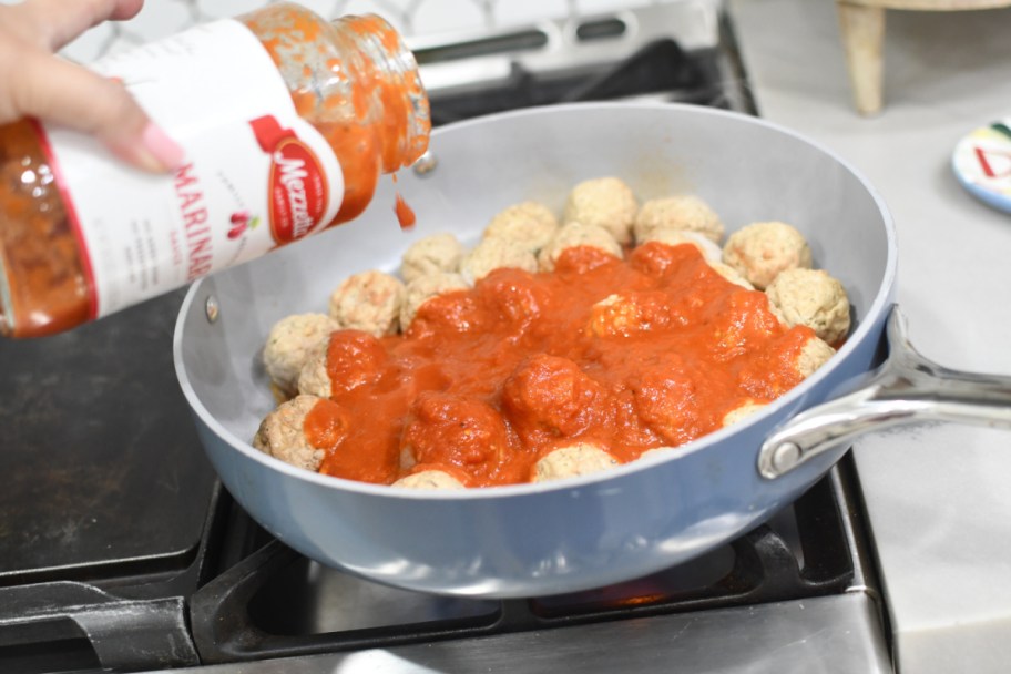 pouring marinara sauce over meatballs in a pot