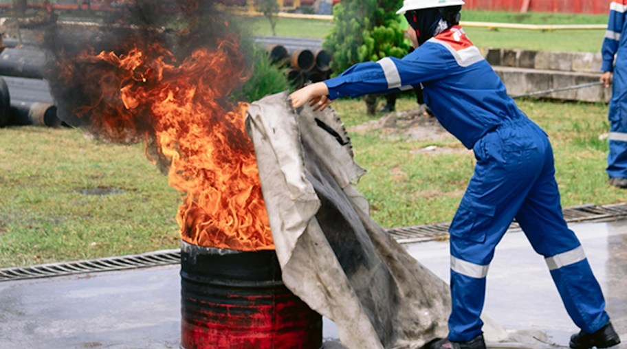 person holding fire blanket over burning bin