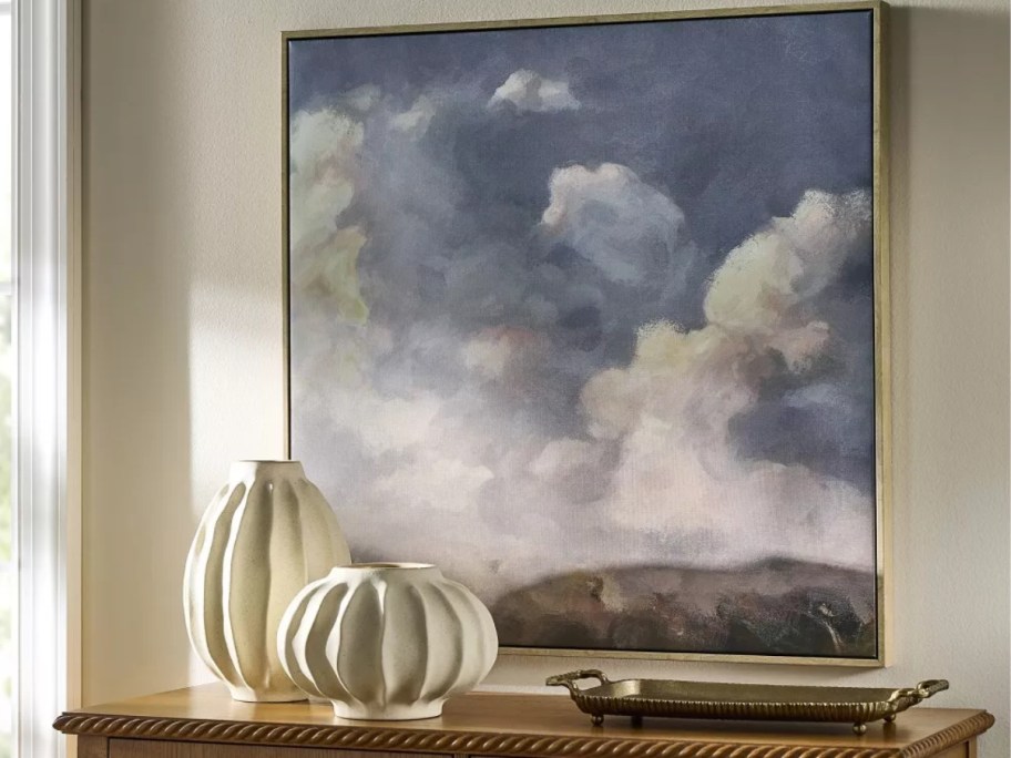 a large framed canvas wall art with clouds on it above a console table