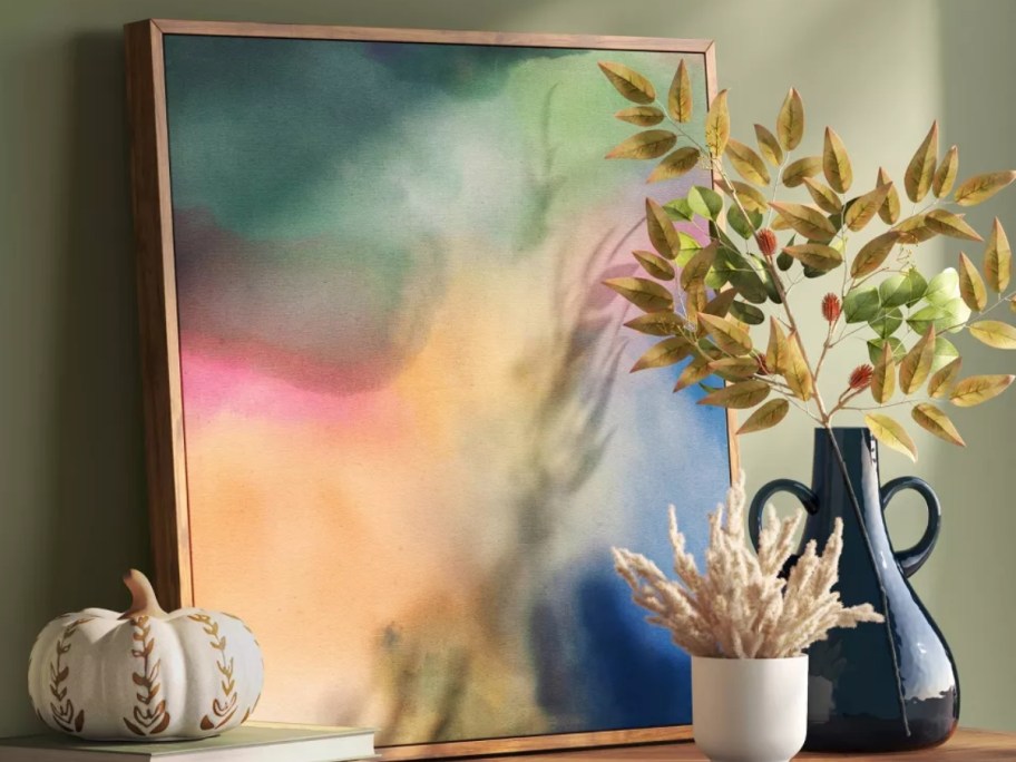a colorful abstract framed wall art piece on a console table with other decor