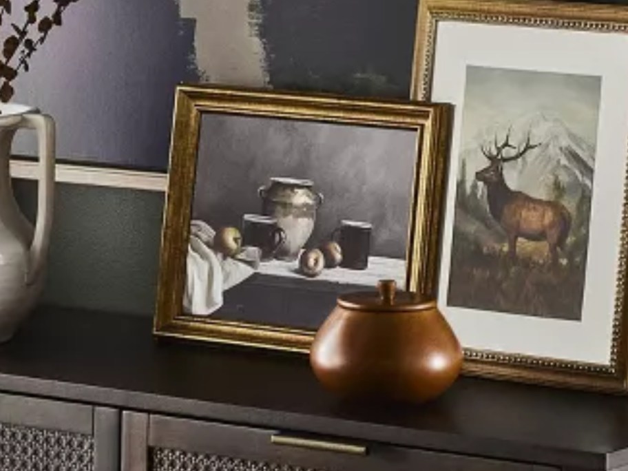 a framed canvas wall art piece with pottery and food sitting on a console table with other decor