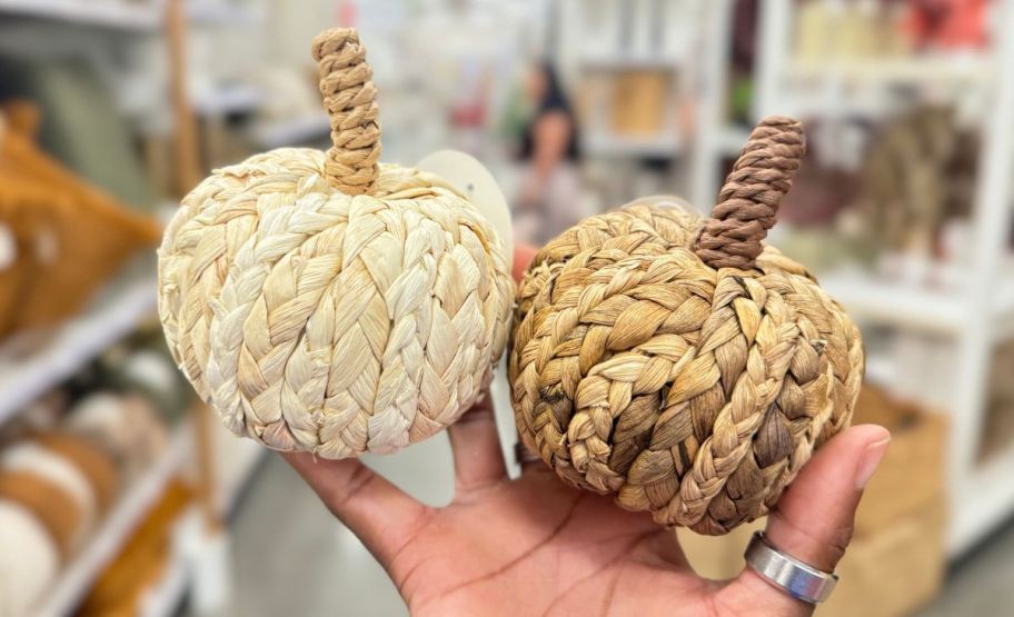 a womans hand holding 2 small woven pumpkins