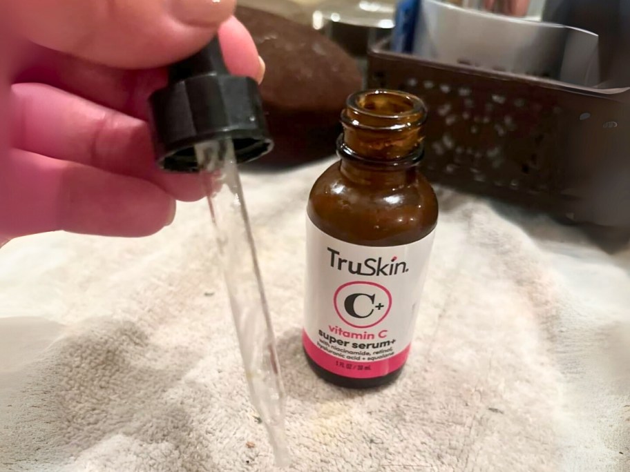 hand holding a dropper with a bottle of TruSkin Vitamin C Super Serum next to it