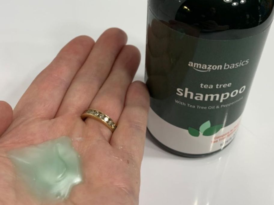 A bottle of Amazon Basics Tea Tree Shampoo with an open hand with some of the shampoo in it