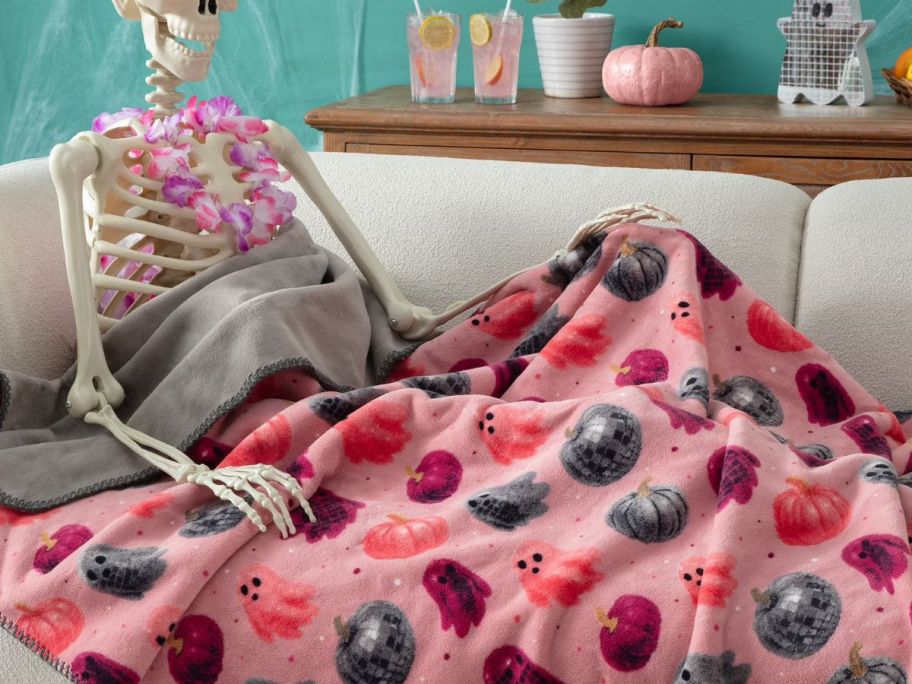 Boo-tique Halloween Reversible Soft Throw Blanket on couch on skeleton's lap