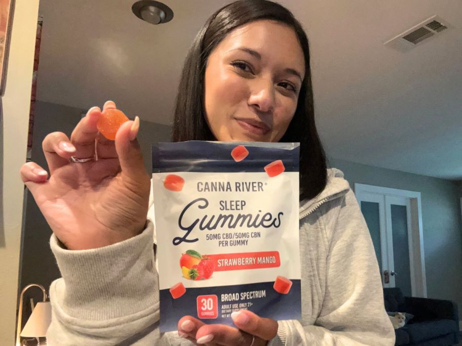 Woman holding a Canna River Gummy in one hand and the whole bag of gummies in the other.