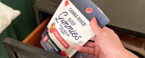 Hand pulling a bag of Canna River Gummies out of a bedside table