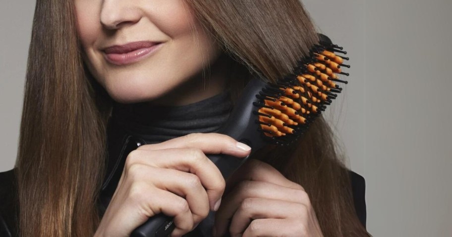 woman with long brown hair using an electric styling brush to style her hair