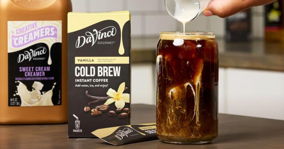 adding cream with iced coffee next to a box of DaVinci Gourmet Vanilla Cold Brew Sticks