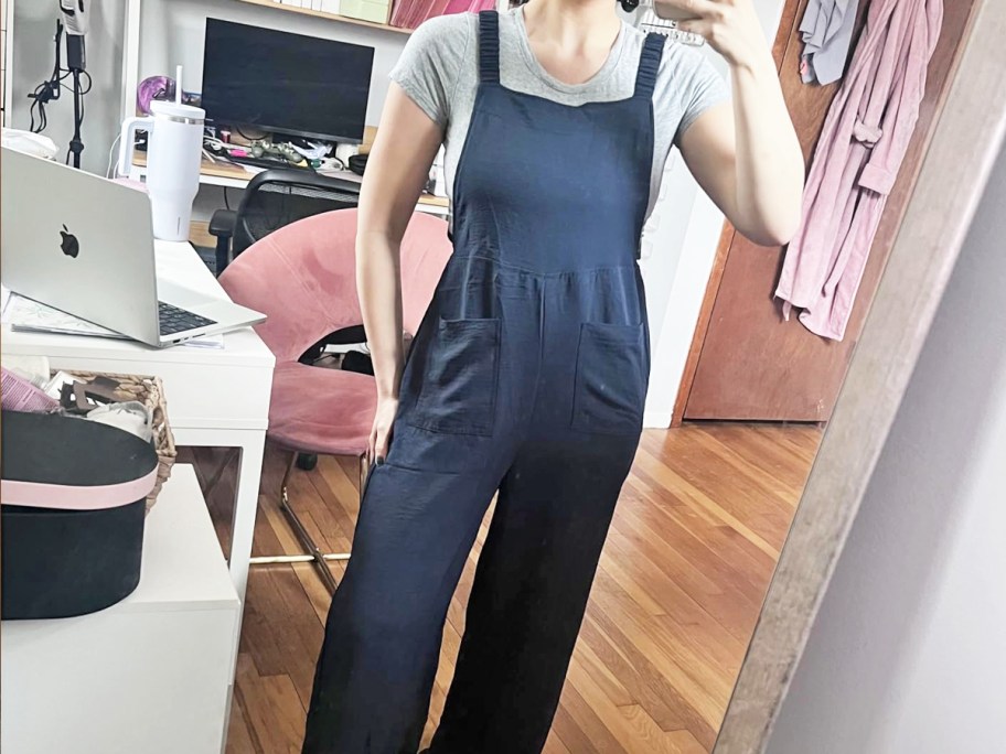 woman wearing a black jumpsuit taking a photo in mirror
