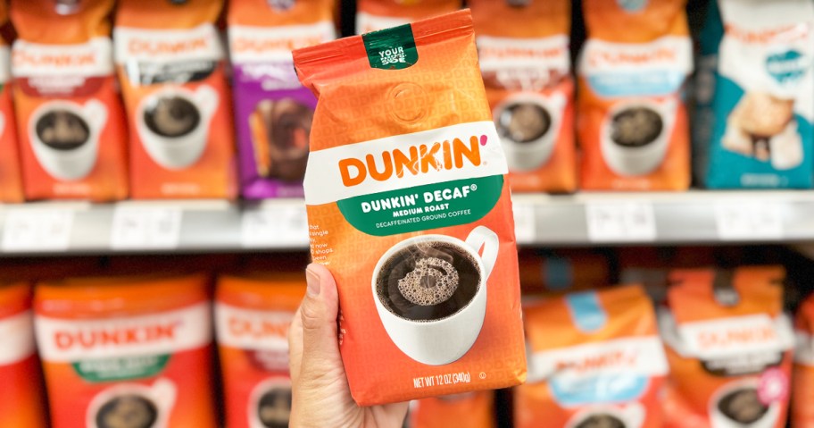 hand holding up an orange bag of Dunkin' Decaf Medium Roast Ground Coffee in store