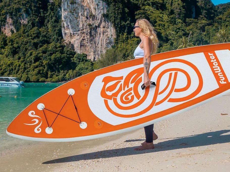 Woman standing on the beach carrying a FunWater padle board