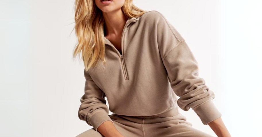 woman wearing a tan half zip wide collar pullover with matching sweatpants sitting down