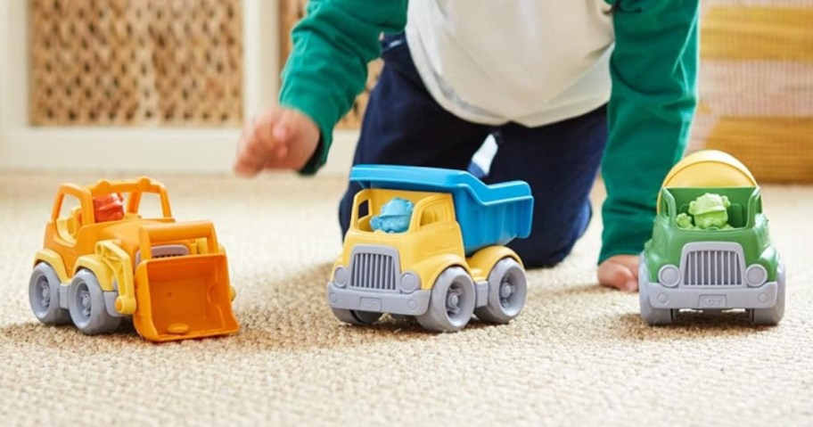 little boy on a living room floor playing with 3 colorful plastic construction vehicles