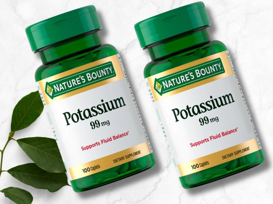 two bottles of Nature’s Bounty Potassium Tablets 99mg 100-Count next to a leaf on a marble background