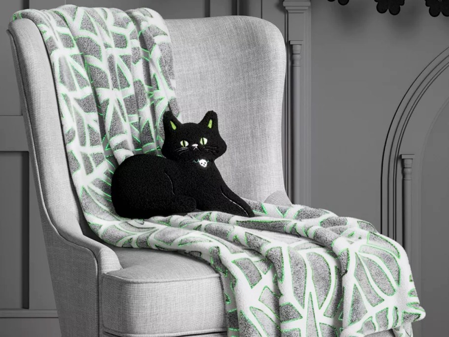 grey spider web print throw blanket on a chair with a black cat throw pillow