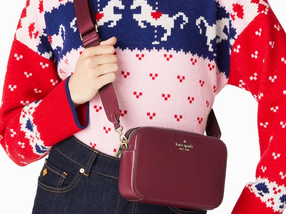 woman in a red, pink, and blue sweater with a maroon crossbody bag