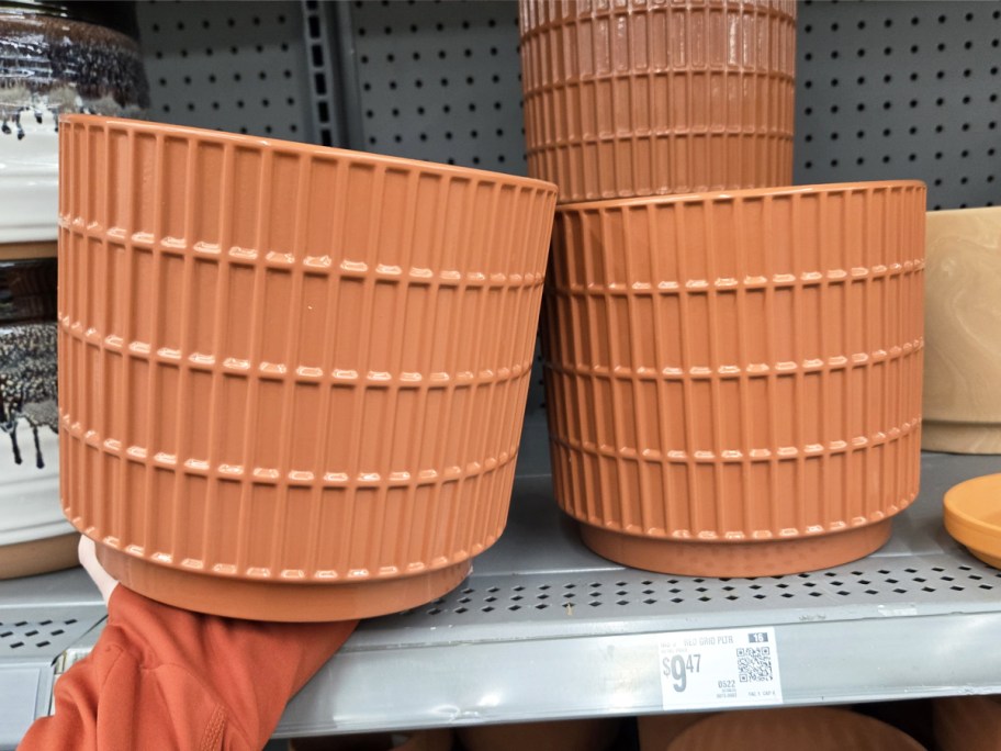 hand holding large grid patterned planter in front of shelf with more