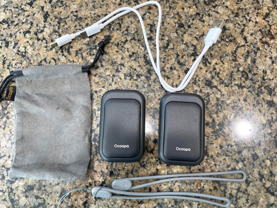 pair of black hand warmers on counter with charging cables