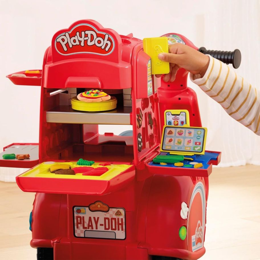 a little kid sliding a pretend credit card on a play-doh pizza delivery scooter