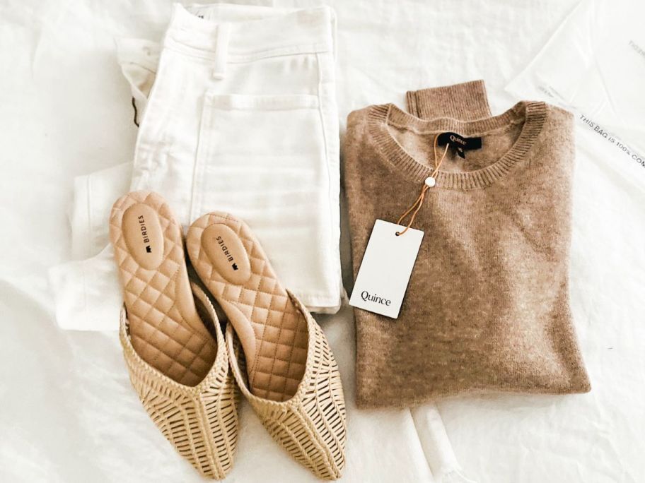 A quince Cashmere sweater on a bed with white pangs and woven mules