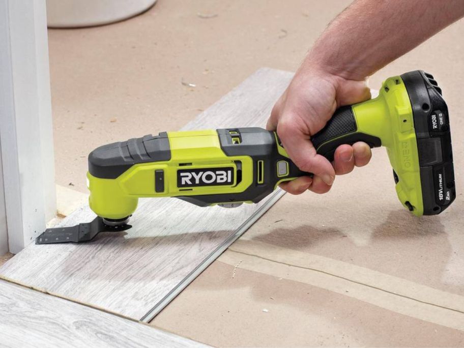 Hand using a Ryobi One+ Multi-tool on a door frame