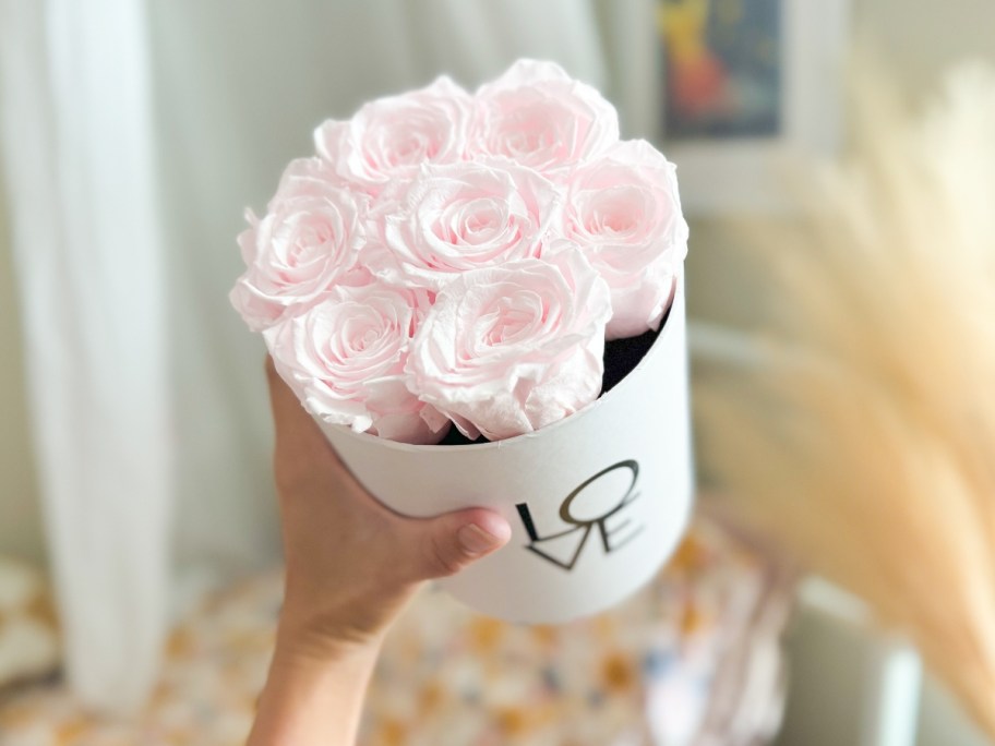 hand holding a round white box with light pink roses in it