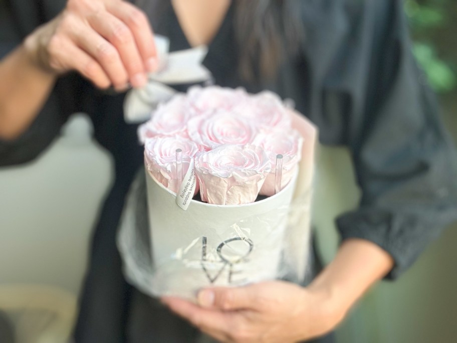 woman pulling a bow off a round white container with light pink roses in it