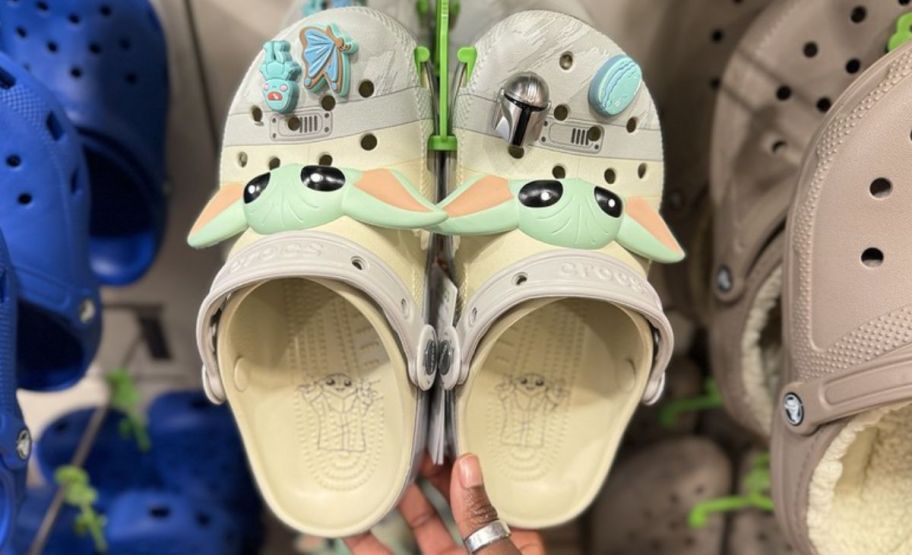 a womans hand holding a pair of Star Wars Grogu crocs Classic Clog