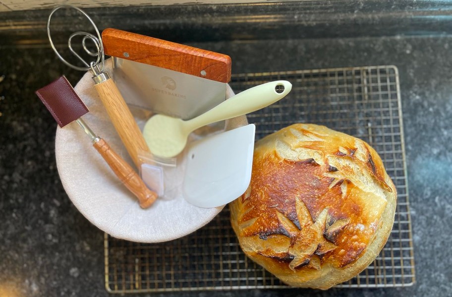 bowl with sourdough baking supplies with loaf of sourdough on cooling rack