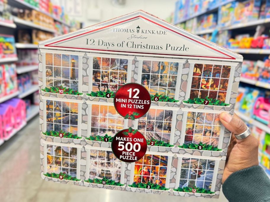 a womans hand holding a thomas kincaid 12 days of christmas puzzle advent calendar