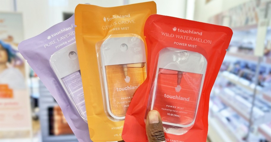 hand holding up three Touchland Hand Sanitizers in store