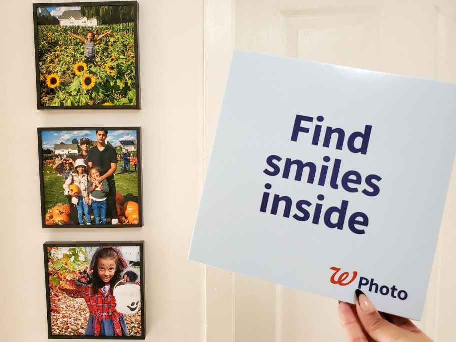 A wall with 3 Walgreens TilePix Photos on it and a hand holding up a Walgreens photo box