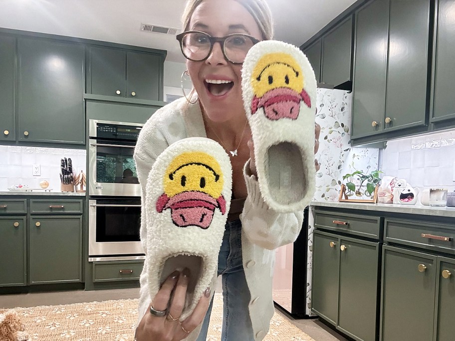 woman holding up a pair of slippers with smiley faces wearing pink cowboy hats on them