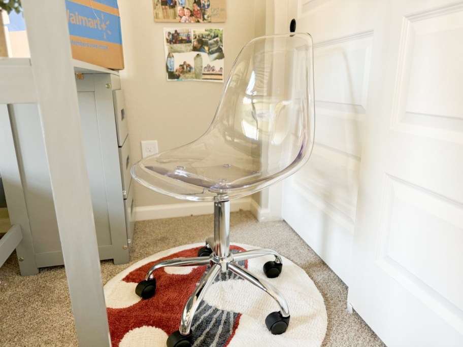 acrylic chair at a desk on top of a mushroom print throw rug with a walmart box in the background