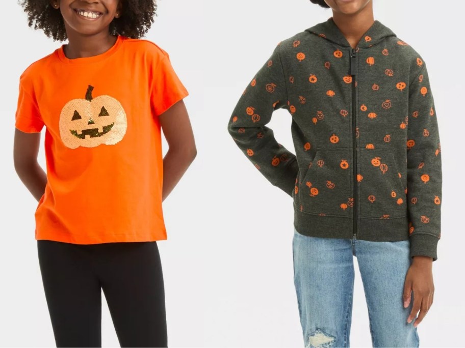 girl wearing an orange Halloween shirt with a sequin pumpkin, and girl wearing a black zip up hoodie with orange jack-o-lanterns