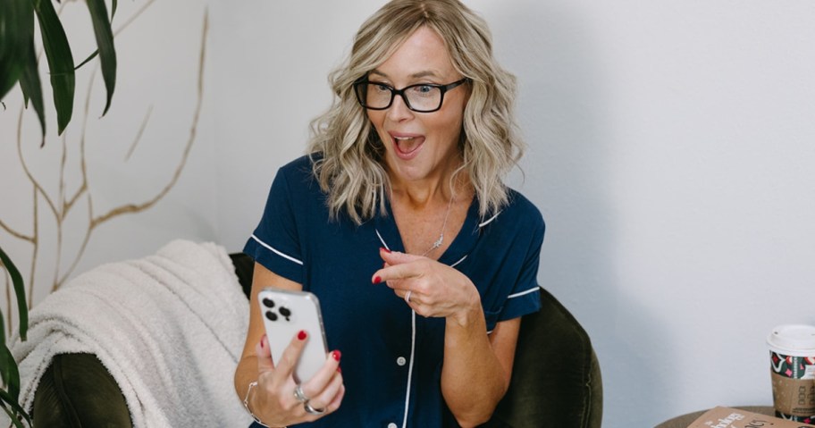 Woman holding up cell phone with one hand and pointing at the screen with her other hand