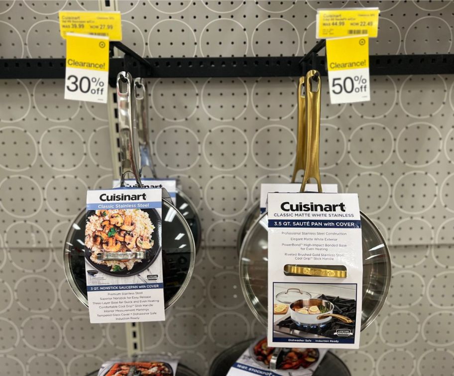 Cuisinart frying pans hanging on a peg board on a store aisle.